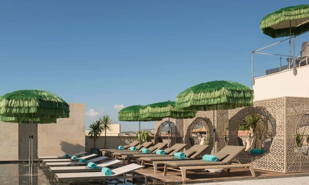 Rooftop infinity pool at El Llorenç Parc de la Mar with green fringed umbrellas and Palma Old Town views — luxury hen weekend rooftop drinks spot.