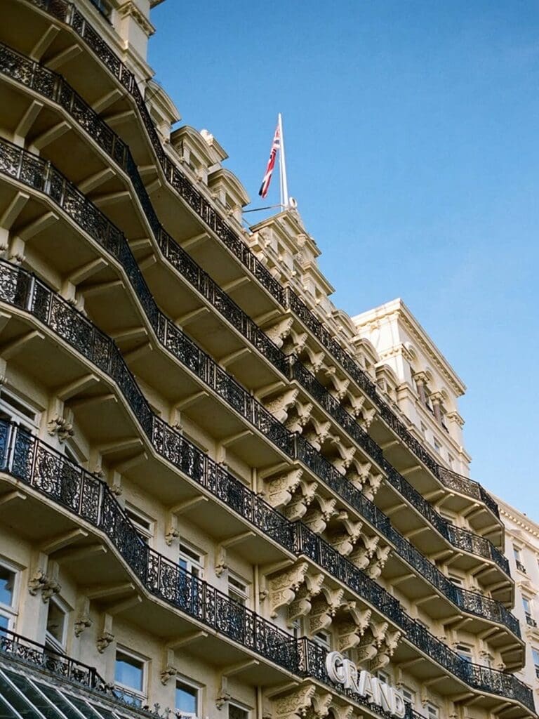 Exterior of The Grand Brighton on the seafront — a grand Victorian frontage with rows of tall windows and balconies facing the promenade, giving “main-character” hen weekend hotel energy.