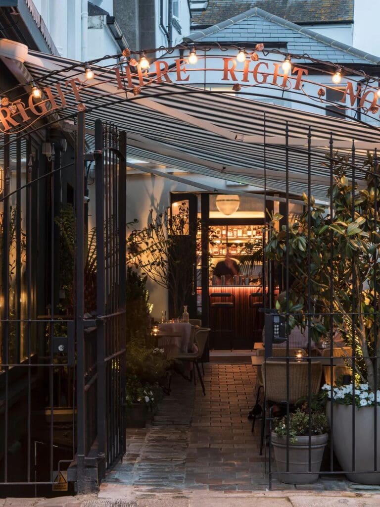 The beautifully lit, inviting entrance of Burnt Orange restaurant in Brighton at dusk, with string lights spelling out its name above a decorative metal gate. This vibey spot is perfect for a special hen weekend dinner.