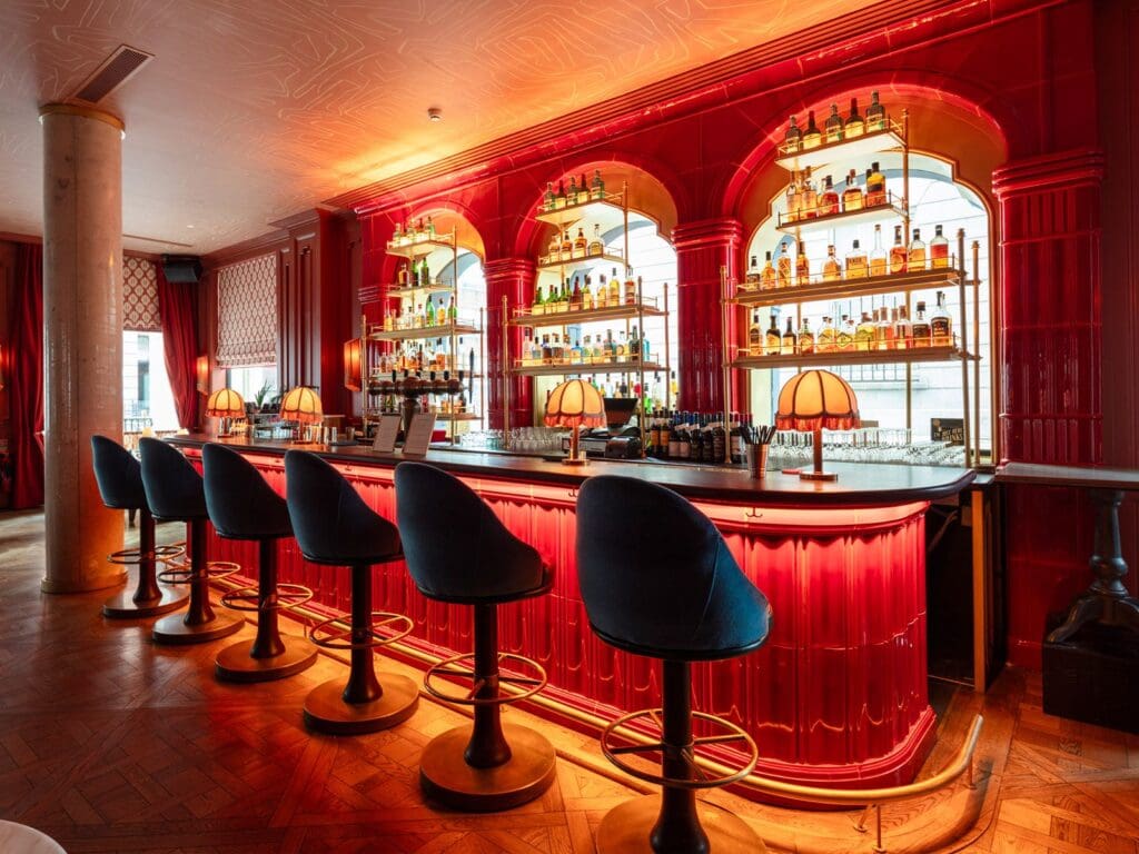 Collins Club bar at The Leinster Hotel in Dublin featuring glossy red tiled arches, illuminated back bar shelving, velvet bar stools and warm lamp lighting, creating a glamorous setting for cocktails before a hen weekend dinner.