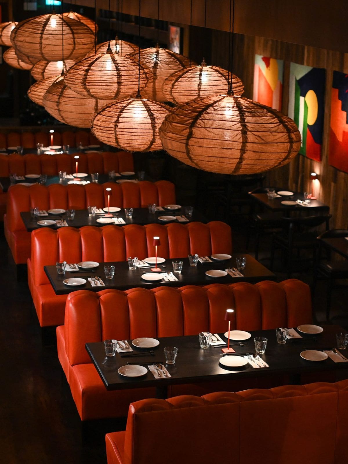 Rows of orange leather booth seating at Kaldero Dublin beneath large woven lantern lights, set for dinner with black tables and minimalist place settings.