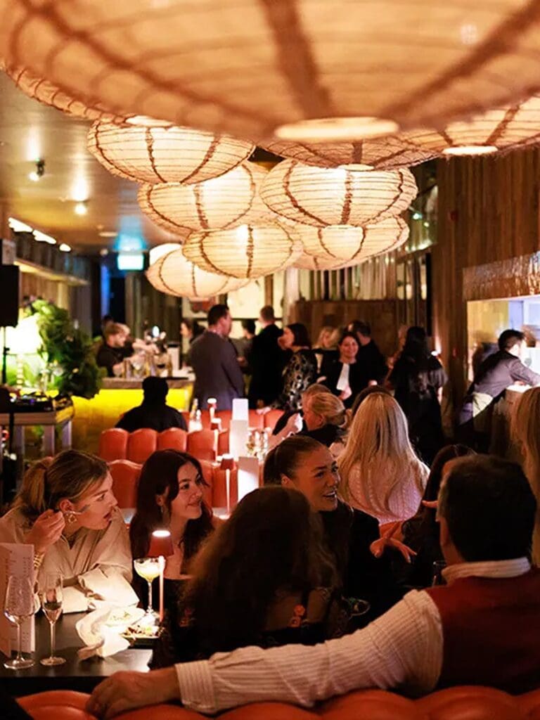 Crowded dining room at Kaldero Dublin with orange leather booths, glowing paper lantern lights and guests enjoying cocktails during a vibey hen weekend dinner.