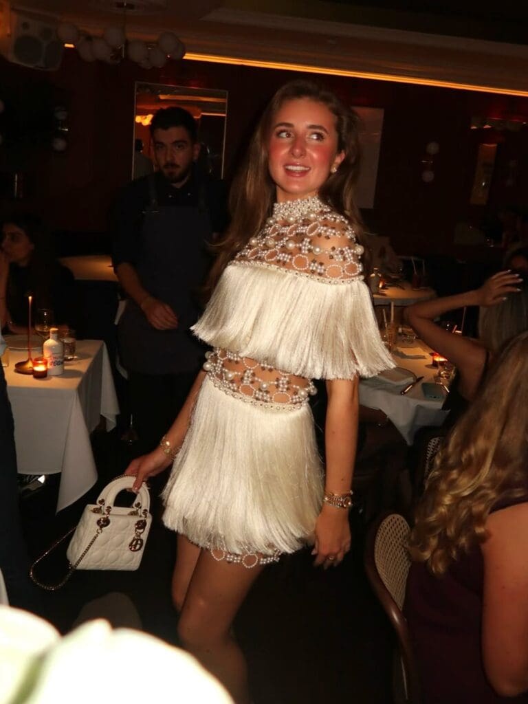 Bride-to-be style moment at Bagatelle in Mayfair, London, with a glamorous white fringe mini dress and lively dinner setting — perfect for a London hen weekend.