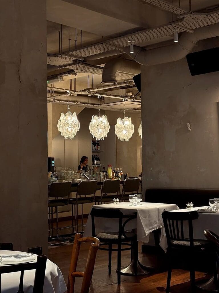 Dining room at Nina in London with white tablecloths, sculptural pendant lights and intimate candlelit tables — an elegant dinner setting for a London hen weekend.