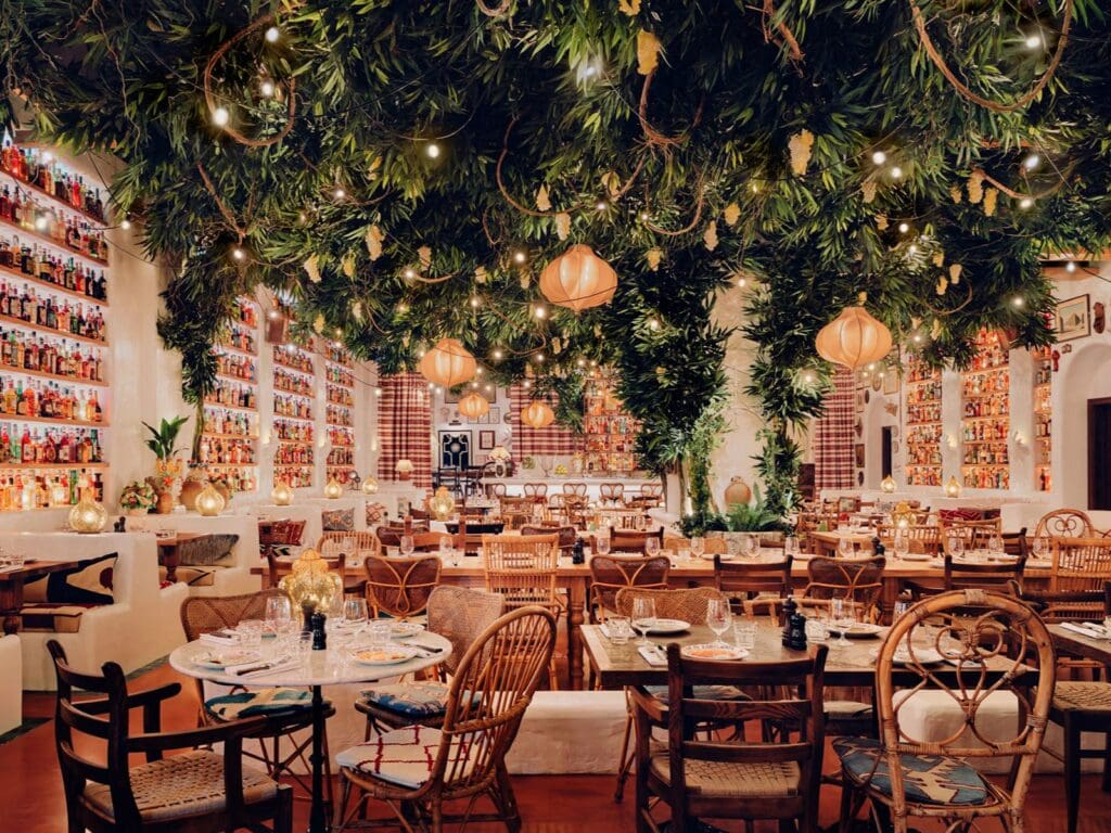 Circolo Popolare Manchester dining room with dramatic greenery-covered ceiling, hanging lantern lights and floor-to-ceiling shelves filled with colourful bottles, set for a lively group dinner.