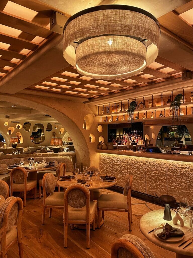 Warm, earthy-toned dining room at Fenix Manchester featuring curved archways, textured plaster walls, woven lighting and an illuminated bar in a stylish evening setting.