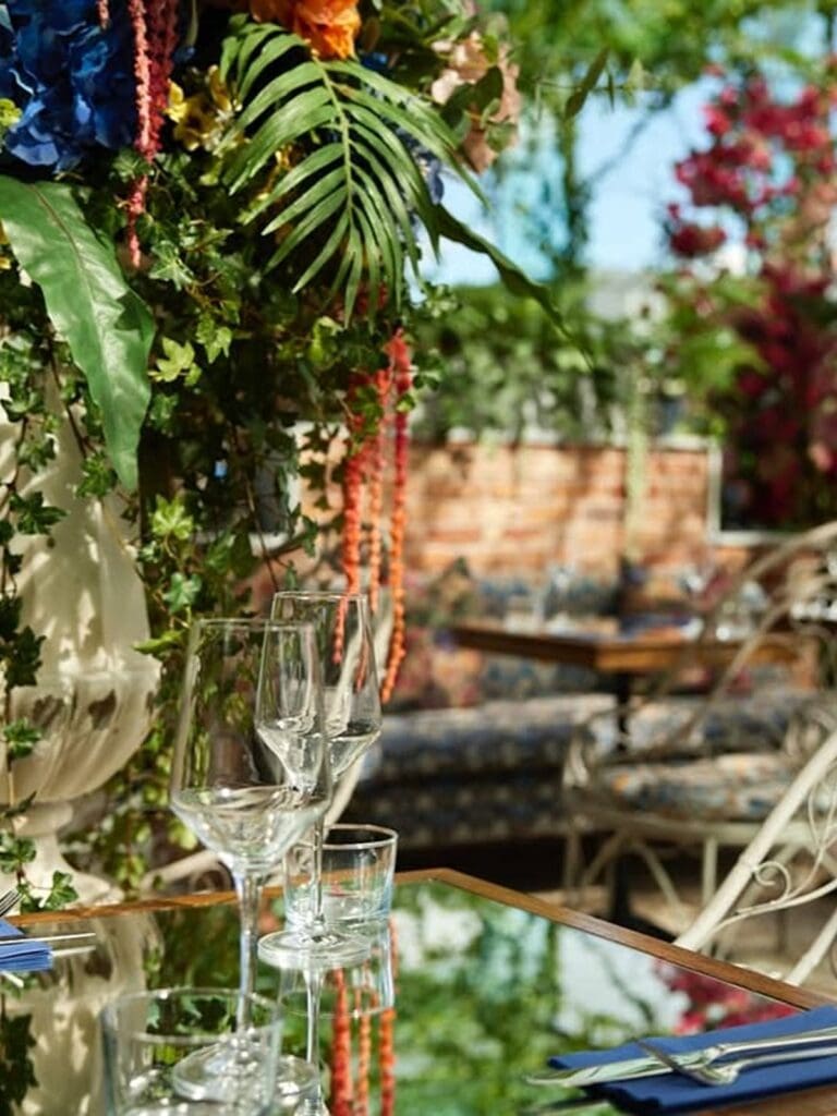 Wine glasses on a mirrored table beneath hanging flowers and greenery at House of Gods’ Sacred Garden rooftop, Glasgow, perfect for a hen weekend brunch.