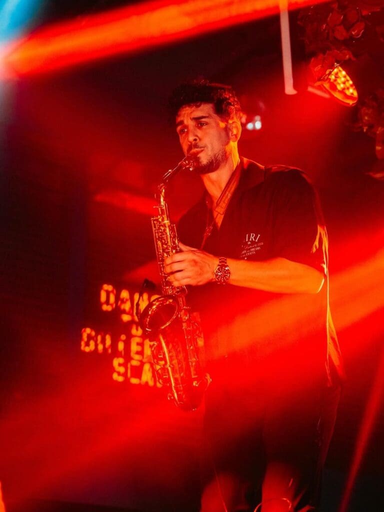 Saxophonist performing under red stage lights at Cirque du Brunch Liverpool, a hen weekend bottomless brunch with live music and big energy.