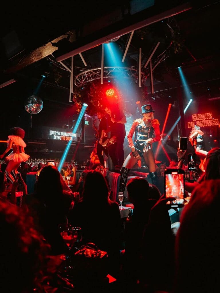 Circus-style performers on stage at Cirque du Brunch Liverpool, with hen weekend tables watching and filming in a club-style bottomless brunch setting.