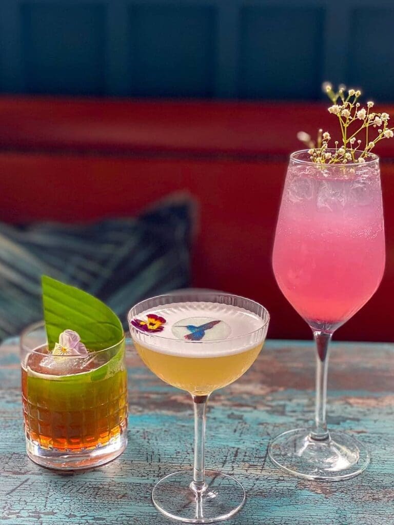 Three colourful cocktails on a distressed blue table at Mason’s Liverpool, a pretty pre-brunch moment for a hen weekend.