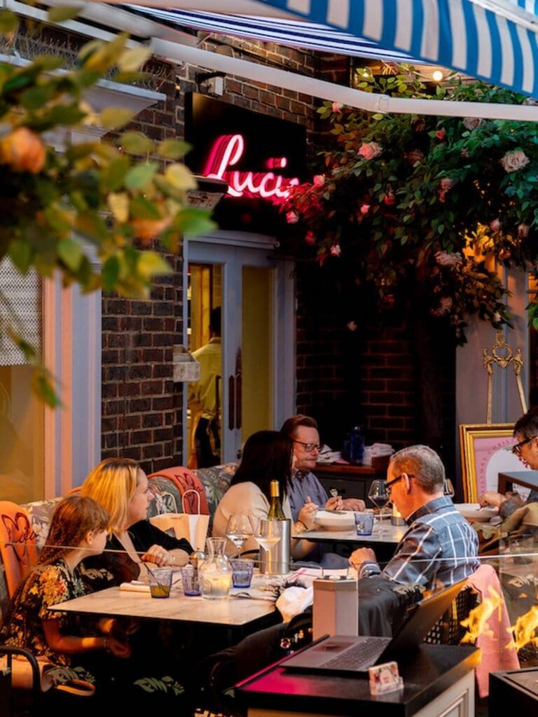 Outdoor terrace at Lucia York with patterned bistro chairs, candlelit tables and diners enjoying an early evening meal, relaxed girls’ weekend energy.