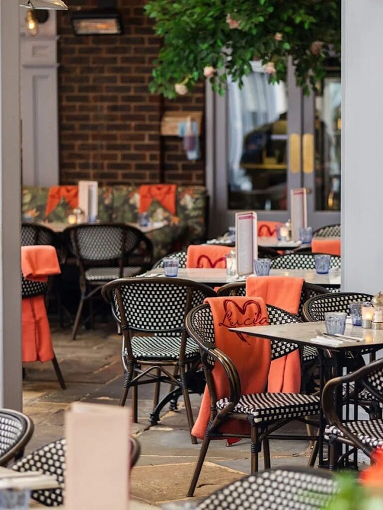 Cosy Italian-style courtyard at Lucia York with greenery, striped awnings and brunch tables set with spritzes, popular for York hen weekends.