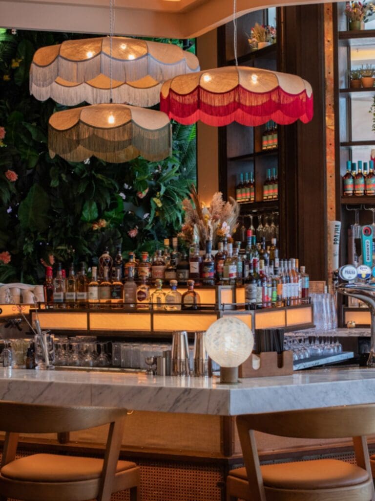 The bar at Palm House, London: tropical plants, glossy tiles and softly lit corners with bottles lined up behind the counter – an atmospheric, photo-worthy spot for cocktails on a girls’ weekend or hen night.