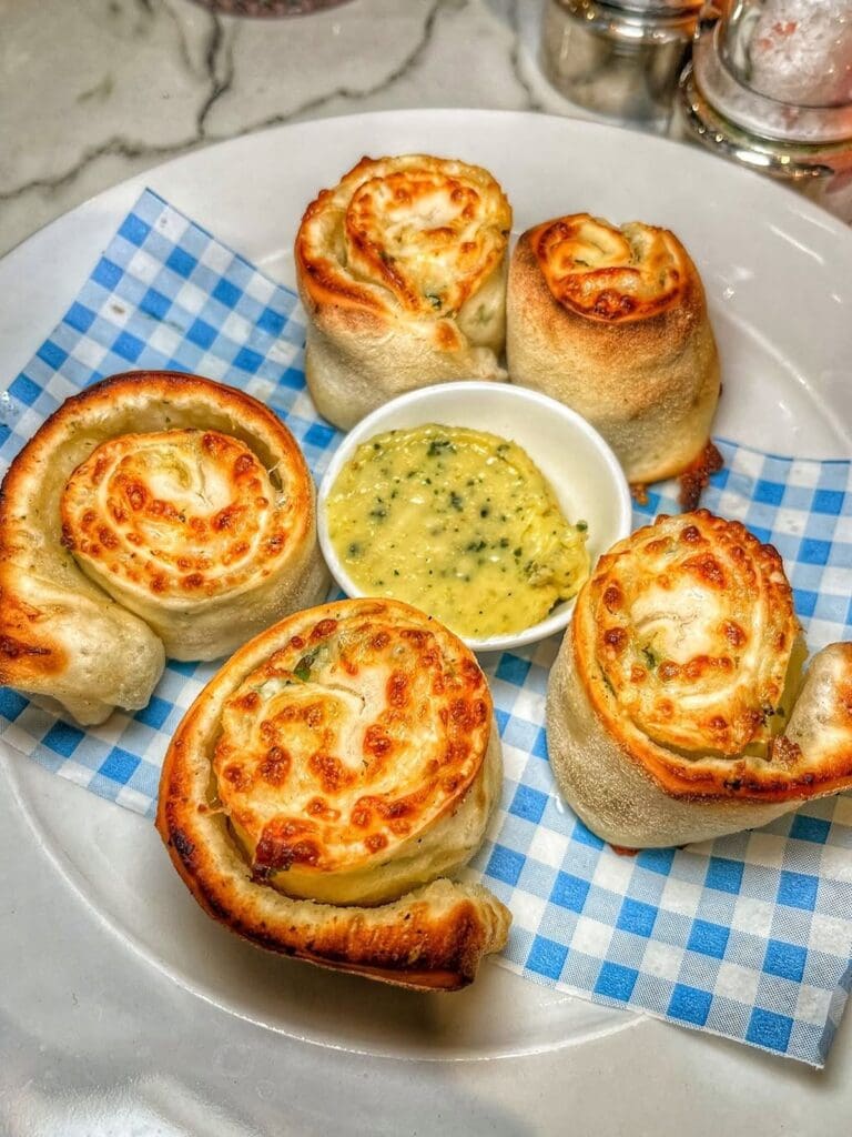A plate of golden cheesy dough balls served on blue and white gingham paper with a small pot of garlic butter dip in the centre, on a marble table at Lucia's in York.