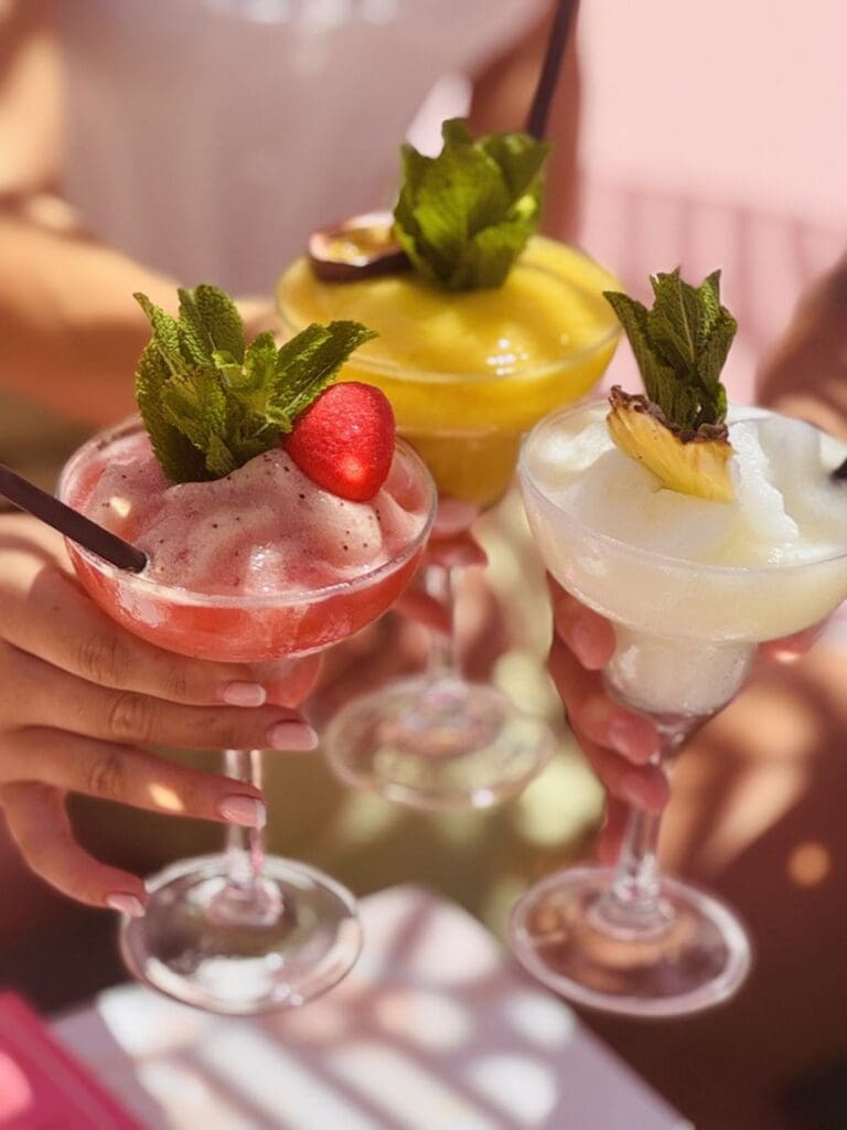 Frozen cocktails with fruit and mint garnishes at Wi-Ki-Woo Ibiza, a pastel beach club bar in San Antonio.