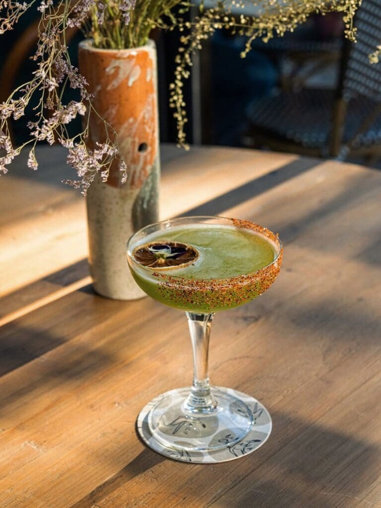 Green cocktail with a chilli-salt rim on a sunlit table at Café Poupette in Palma, a relaxed brunch stop for a hen weekend.