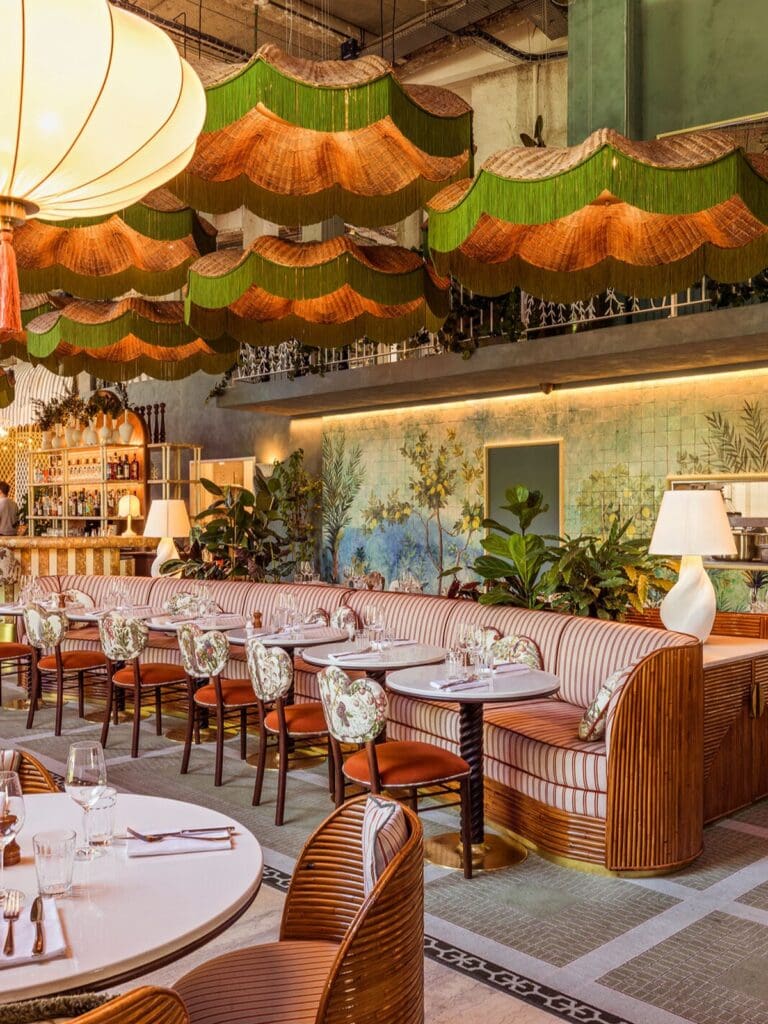 Bright, design-led Paris restaurant interior with curved banquettes, patterned chairs and statement green lampshades, set up for a long lunch with friends.