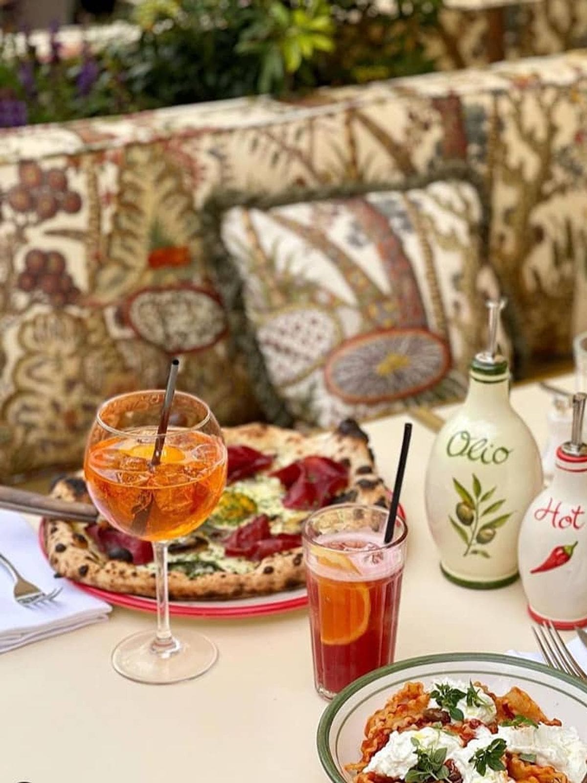 Spritz cocktails and pizza on a Paris restaurant table with patterned banquettes and greenery, capturing a relaxed boozy lunch moment on a girls’ weekend.