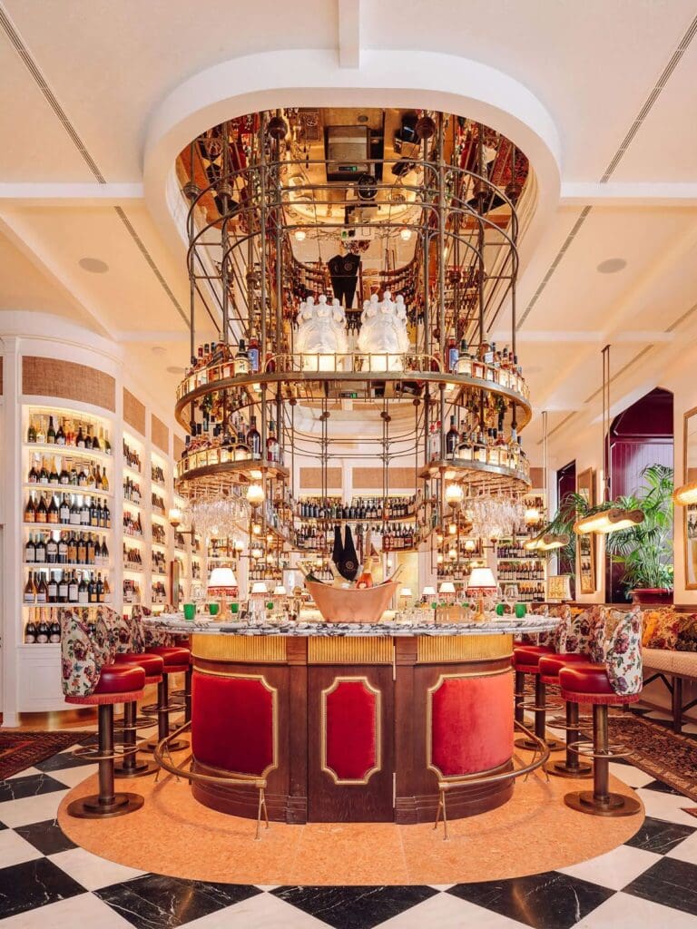 Statement circular bar at Rocco Lisbon with red velvet stools, marble countertop and dramatic tiered wine display rising to the ceiling, creating a glamorous setting for a vibey hen weekend dinner.