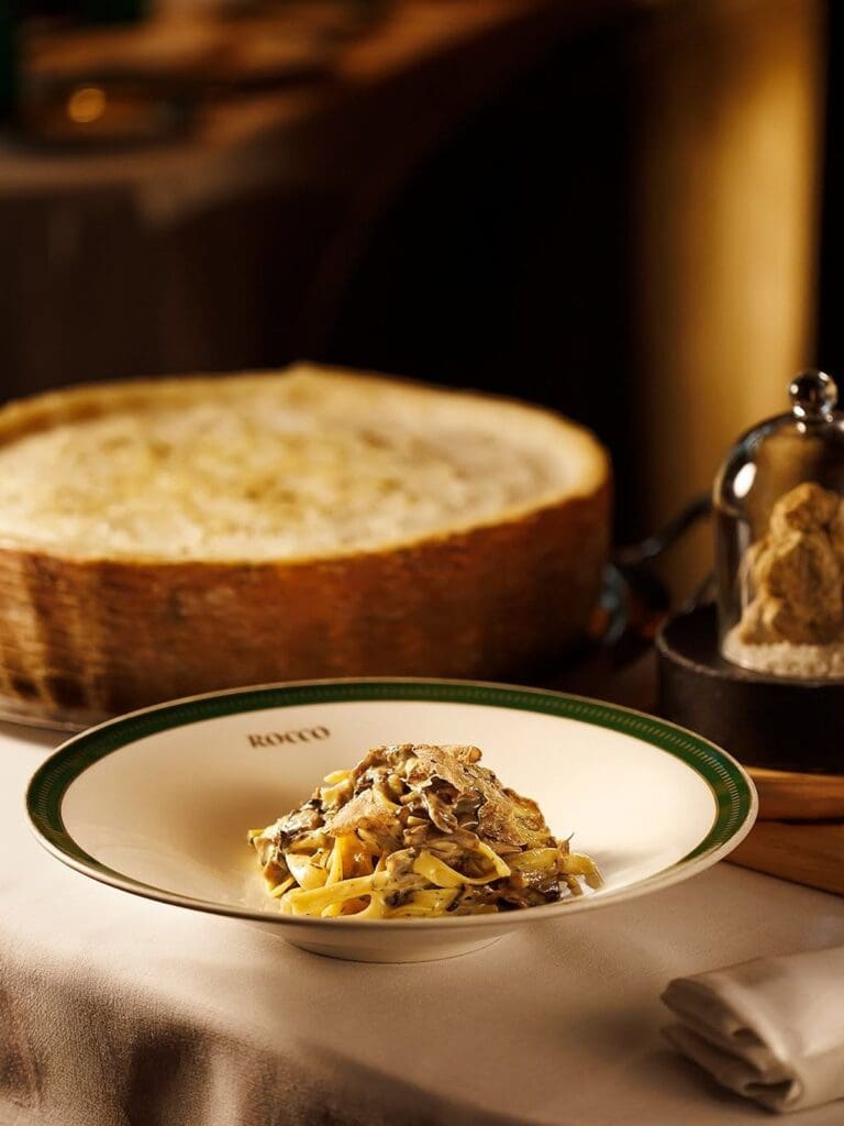 Fresh tagliatelle topped with shaved truffle served at Rocco Lisbon, plated on white china with a large wheel of cheese in the background during a luxurious hen weekend dinner.
