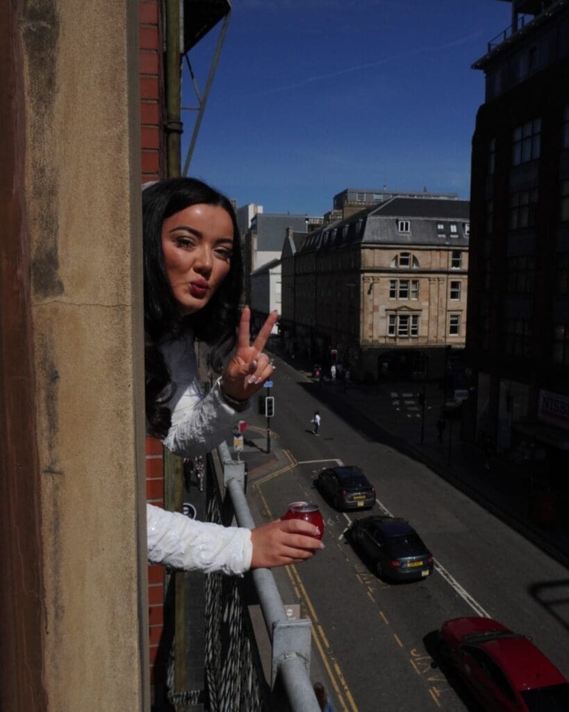 Bride to be soaking up the sun on a Glasgow hen weekend, drink in hand and city below — the kind of carefree moment every girls trip needs.