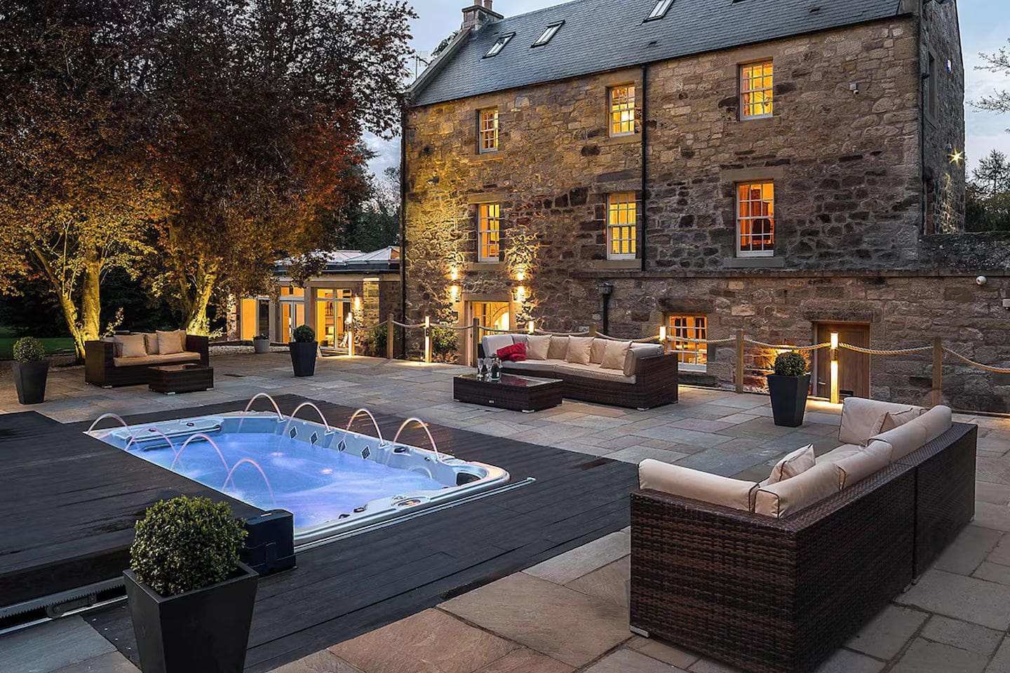 Outdoor terrace at The Old Mill House Experience near Edinburgh with hydro spa pool, garden seating and restored stone house exterior at dusk