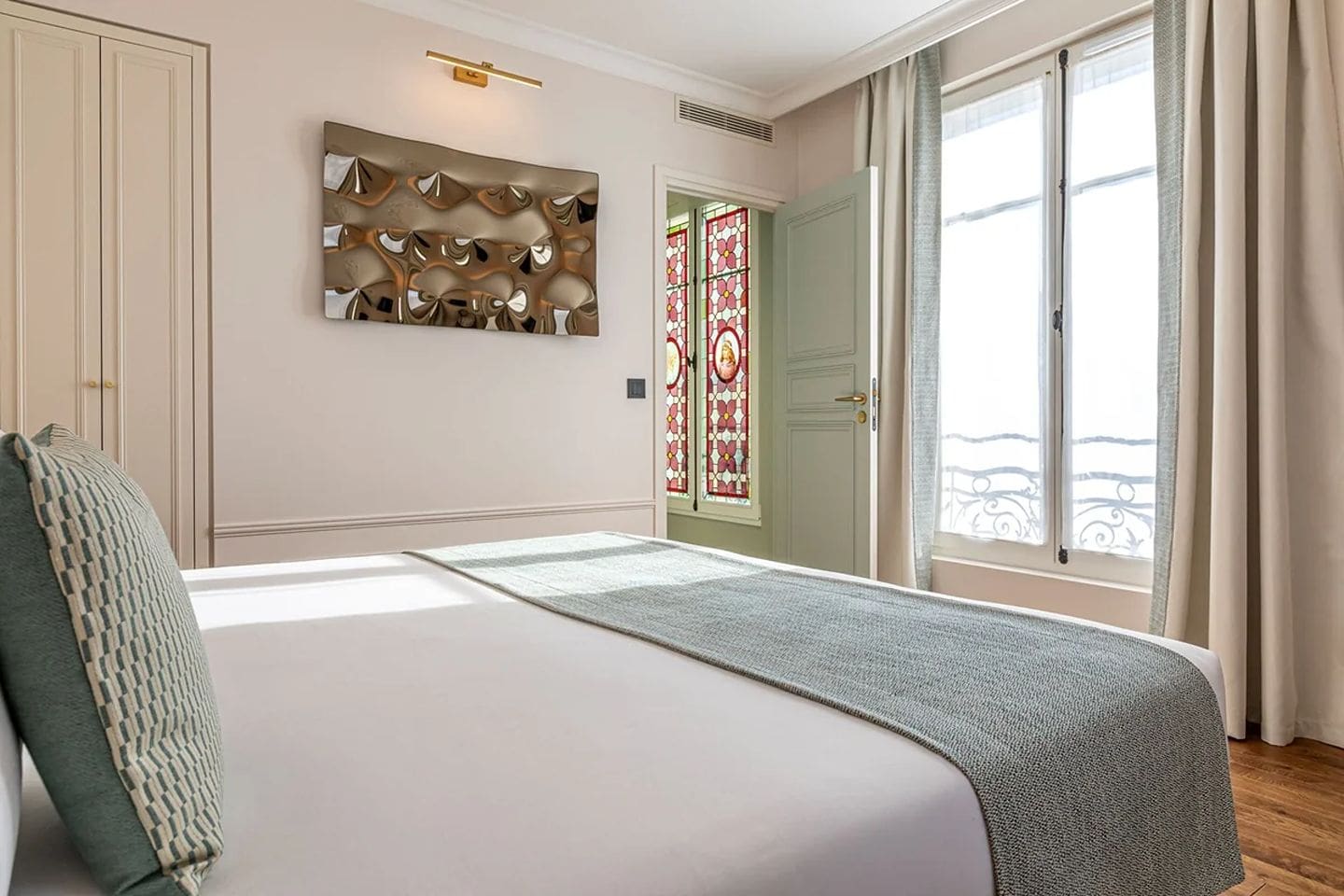Paris rooftop apartment dining table with balcony views over classic Haussmann rooftops, alongside a bright bedroom with soft neutral tones and stained glass detail