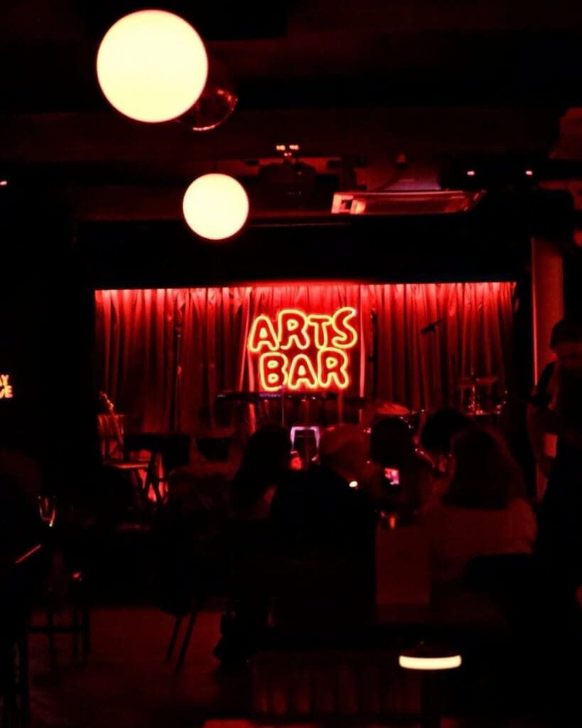 Red neon Arts Bar sign glowing above a small stage in Liverpool, with low lighting and a live music feel for a cool girls’ night out in Liverpool.