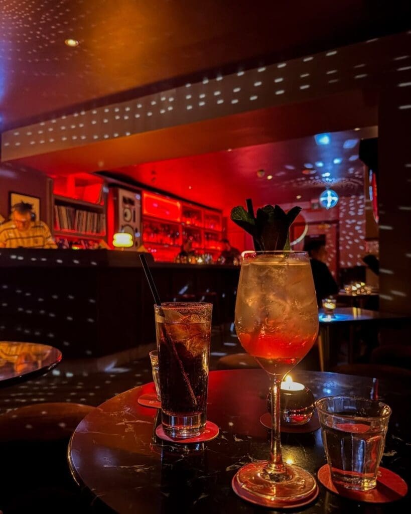 Cocktails on a low-lit table inside Simone’s Cocktail Club in Liverpool, with red bar lighting, disco-ball reflections and listening-bar energy for a cool girls’ night out in Liverpool.