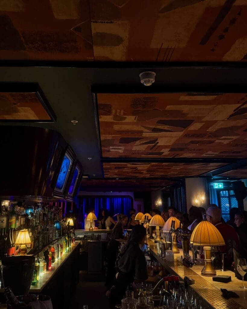 Low-lit bar at Mollie’s Manchester, with glowing table lamps, bottles behind the bar and a busy evening crowd for a polished girls’ night out in Manchester.