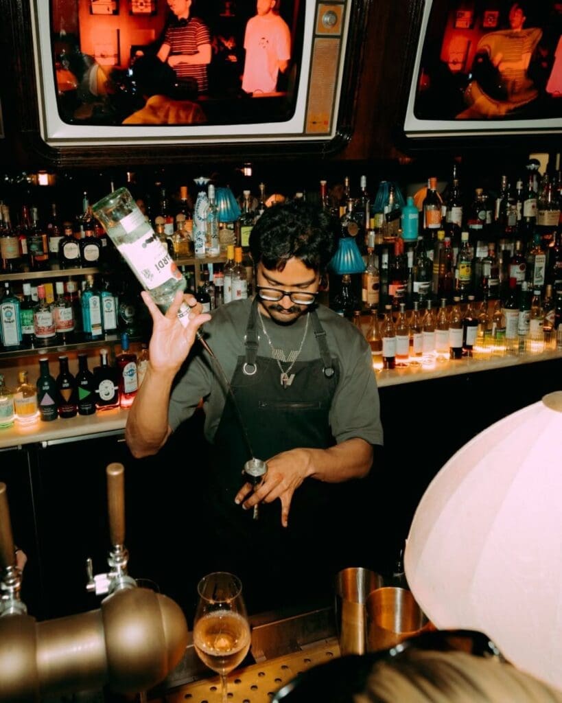 Bartender mixing cocktails behind the bar at Mollie’s Manchester, with glowing back-bar bottles, soft lamp lighting and a lively girls’ night out atmosphere.