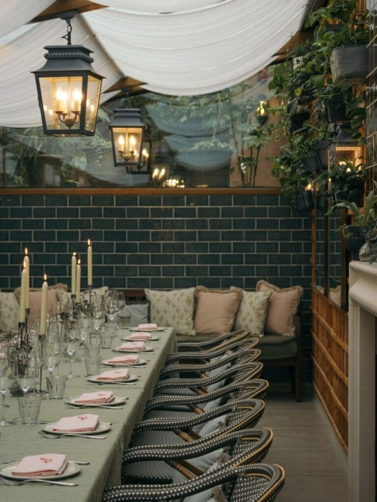 Private dining table in The Courtyard in Gleneagles Townhouse with pink napkins, candles and bistro chairs under draped fabric and lanterns, a stylish option for Edinburgh hen do activities.