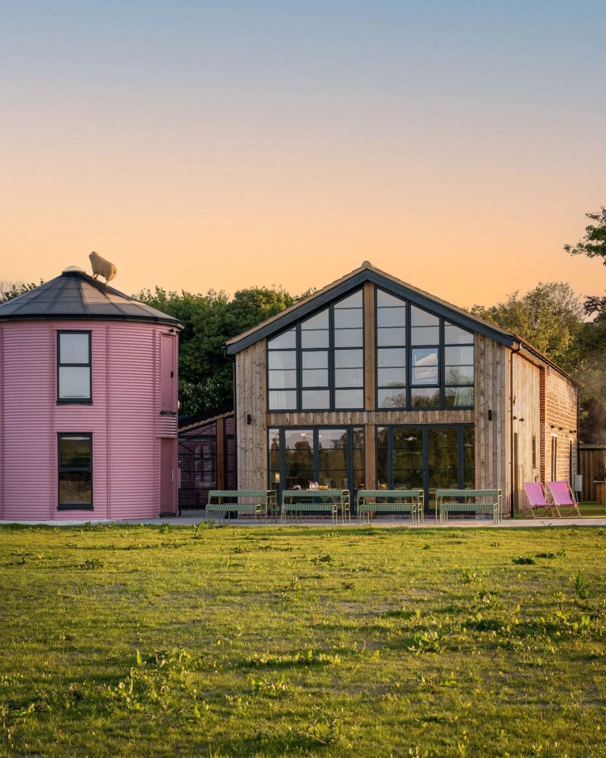 Exterior of Hesdin Estate at sunset featuring modern barn-style architecture and a pink silo building set within open countryside — a design-led rural retreat for large group stays and luxury hen weekends.