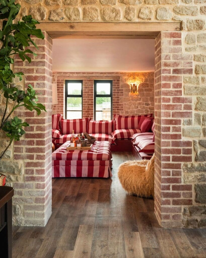 Cosy lounge at Hesdin Estate with red striped banquette seating, exposed brickwork and country house interiors designed for long evenings in — a luxury group stay for hen weekends and girls’ trips.