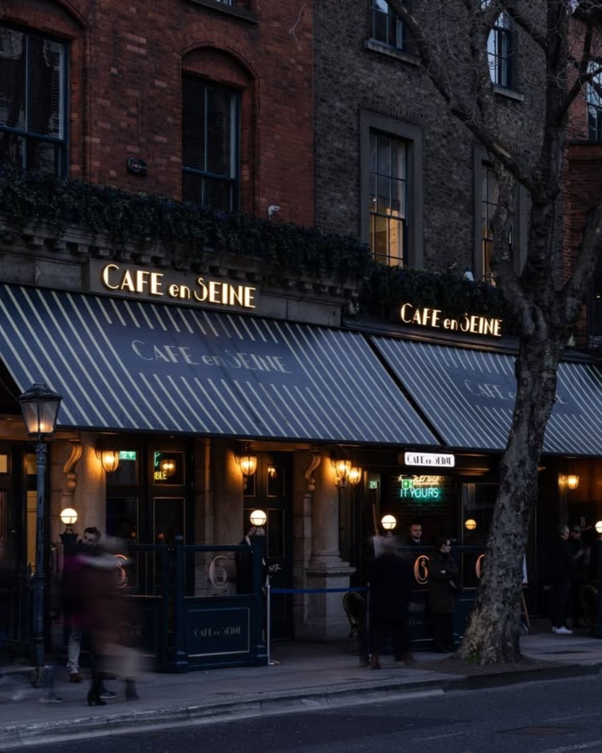 The illuminated exterior of Café en Seine in Dublin at dusk, its striped awnings and grand facade setting the scene for cocktails, late-night drinks and a stylish Dublin hen weekend.