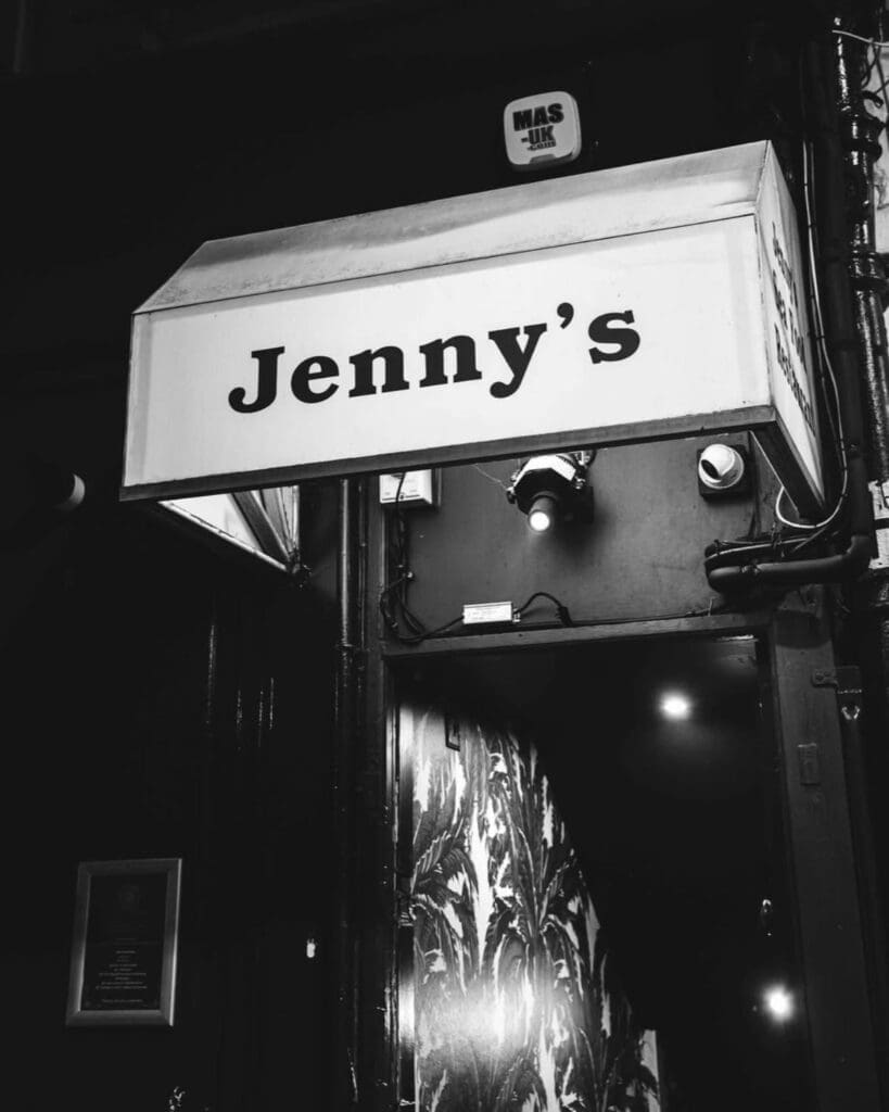 Black-and-white exterior of Jenny’s Bar in Liverpool, with its illuminated entrance sign marking the hidden late-night cocktail spot for a Liverpool hen weekend.