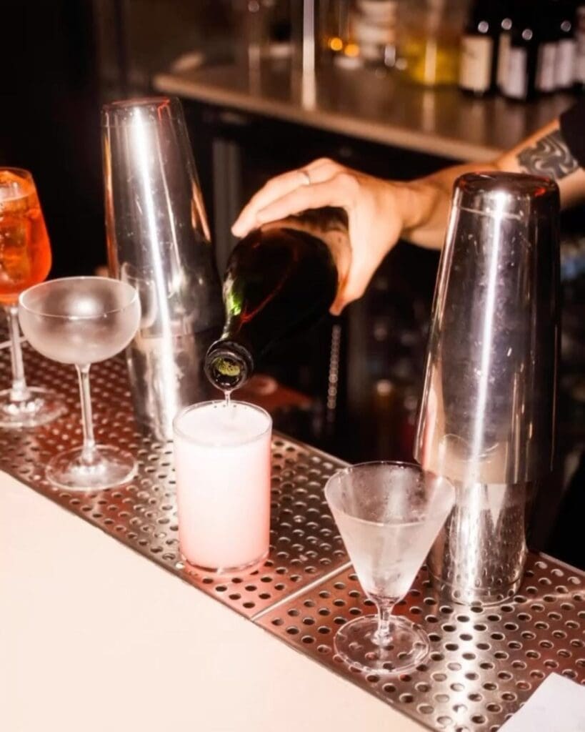 Bartender pouring a drink at Sister Ray in Liverpool, with cocktails and polished metal shakers lined up across the bar for a stylish hen weekend night out.