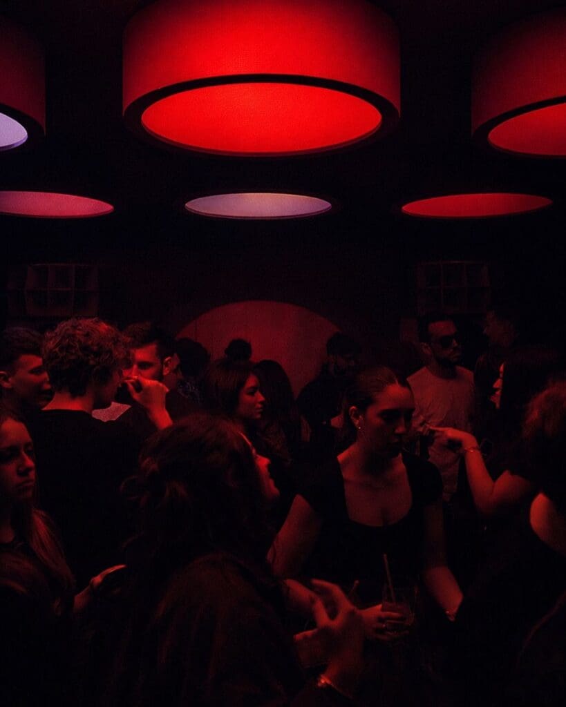 Dimly lit crowd inside Suono in Liverpool, with red overhead lighting and guests gathered on the dance floor during a late-night hen weekend out.