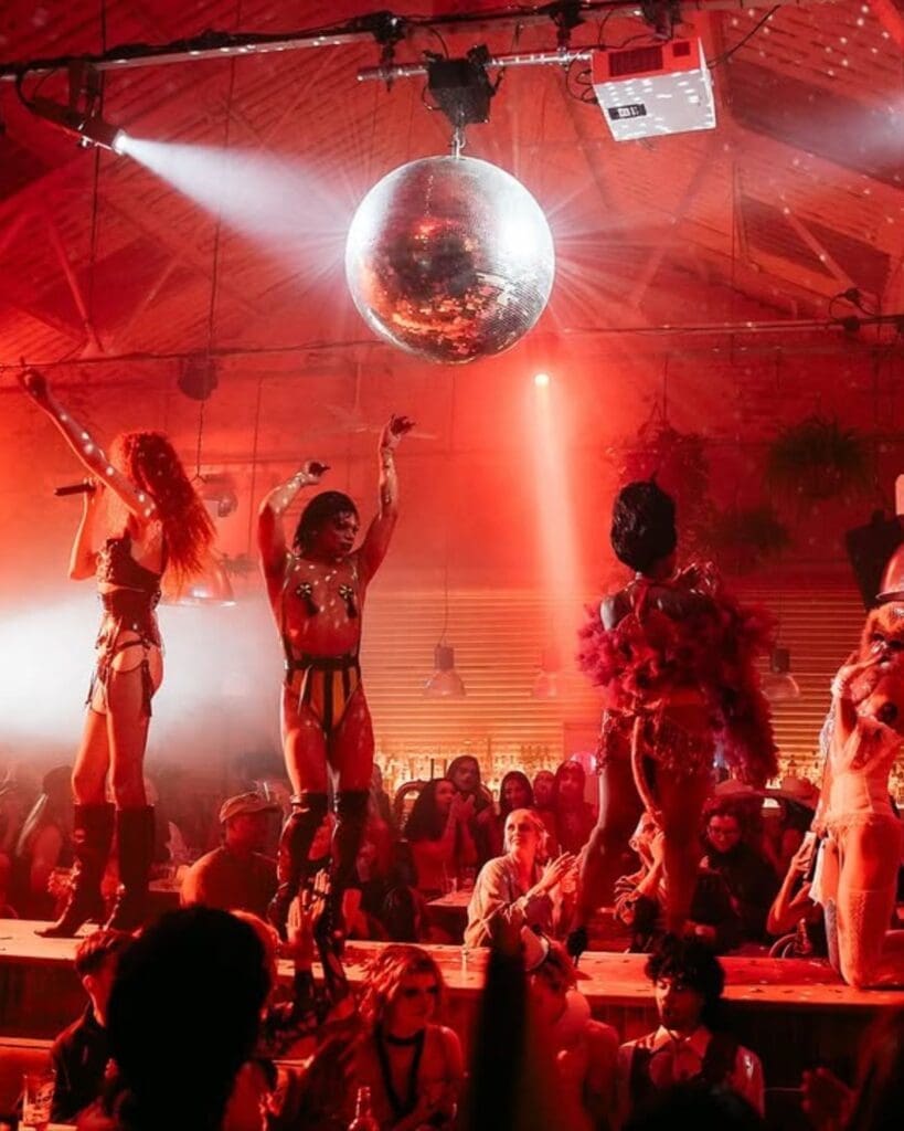 Performers on stage beneath a giant disco ball at The Firehouse in Manchester, surrounded by a packed crowd and red late-night lighting — a theatrical spot for going out-out on a Manchester hen weekend.