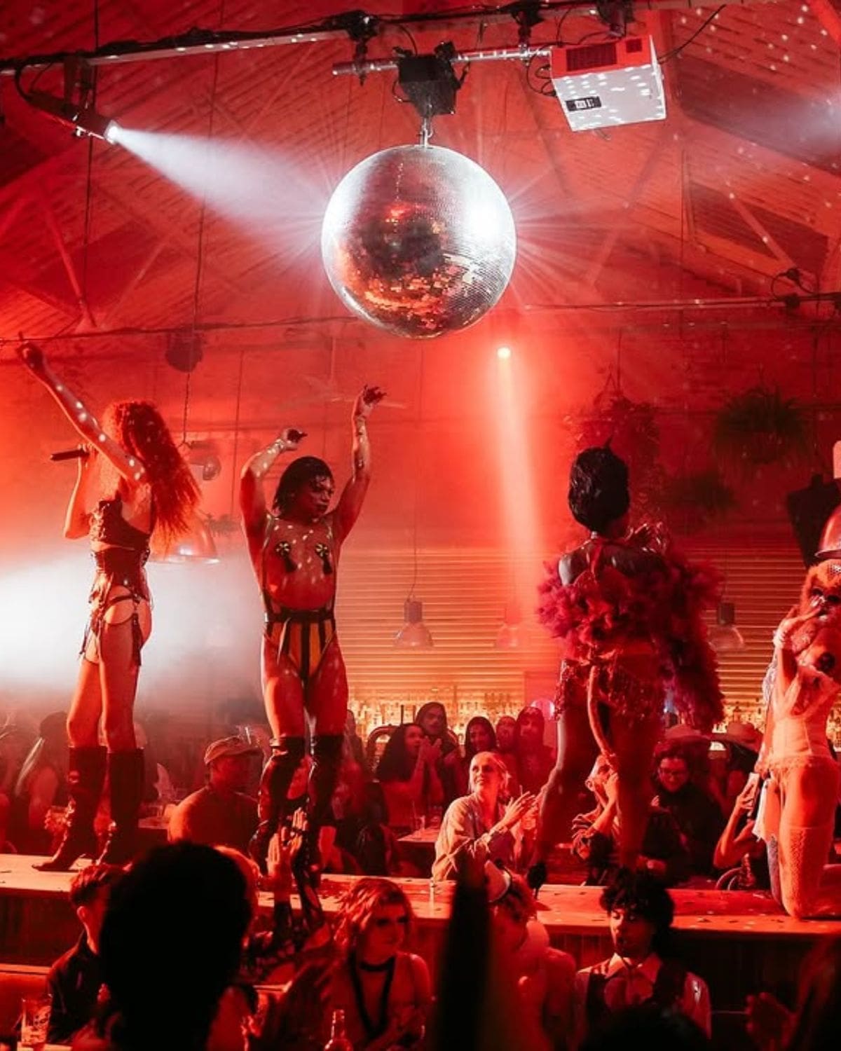 Performers on stage beneath a giant disco ball at The Firehouse in Manchester, surrounded by a packed crowd and red late-night lighting — a theatrical spot for going out-out on a Manchester hen weekend.
