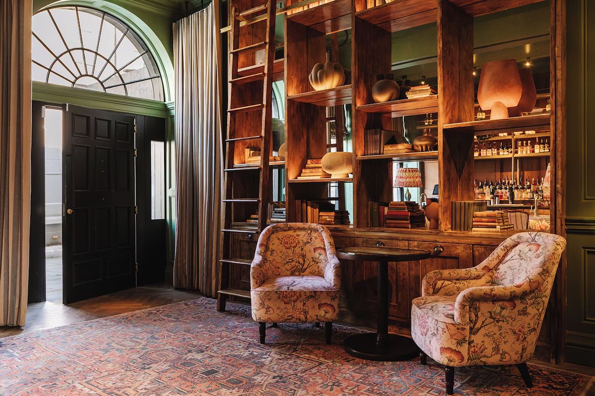 Stylish lobby at The Dean Dublin, a central Dublin hen weekend hotel with dark green walls, statement shelving and patterned armchairs.